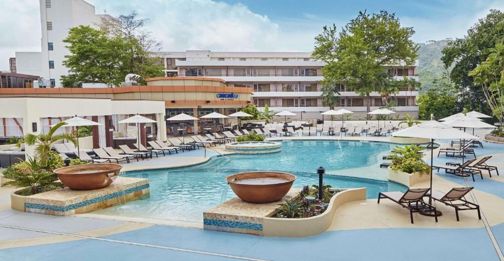 una imagen de una piscina de hotel con sillas y sombrillas en Hilton Trinidad & Conference Centre en Puerto España