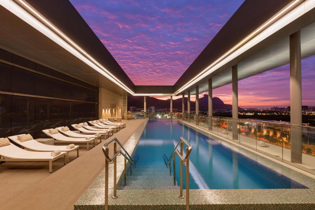 a hotel swimming pool with lounge chairs and a sunset at Hilton Barra Rio de Janeiro in Rio de Janeiro