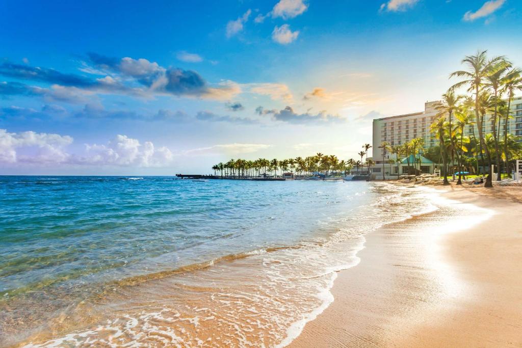 a beach with a hotel and palm trees and the ocean at Caribe Hilton in San Juan