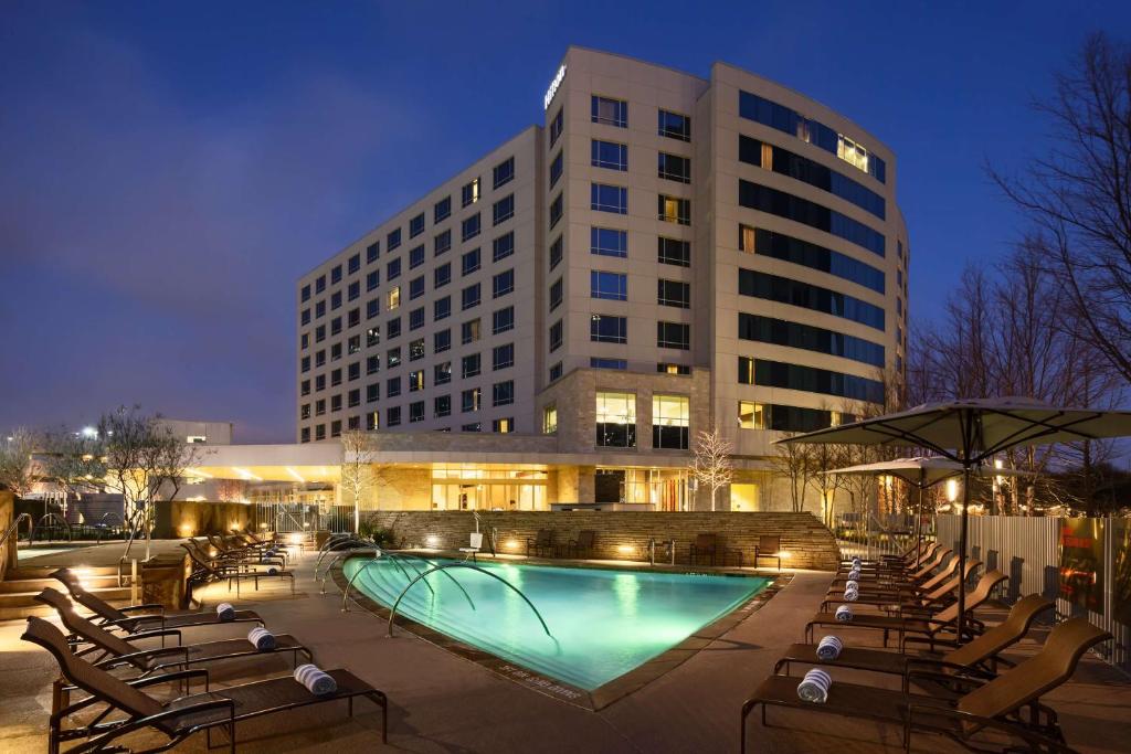 un hôtel avec une piscine, des chaises et un bâtiment dans l'établissement Hilton Dallas/Plano Granite Park, à Plano