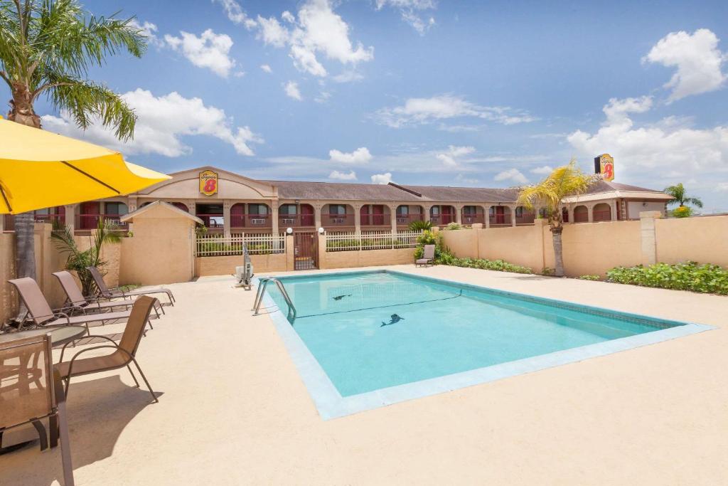 a pool with chairs and an umbrella and a building at Super 8 by Wyndham Kingsville in Kingsville