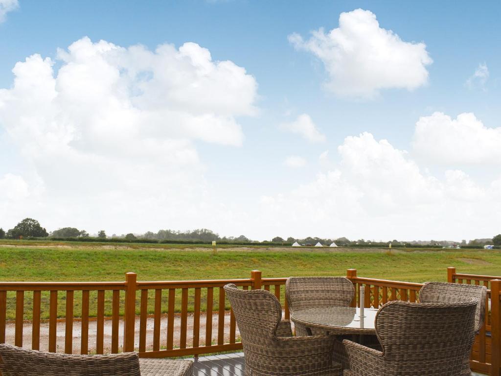 eine Terrasse mit Stühlen, einem Tisch und einem Feld in der Unterkunft Lodge 69 in Stonham Aspall