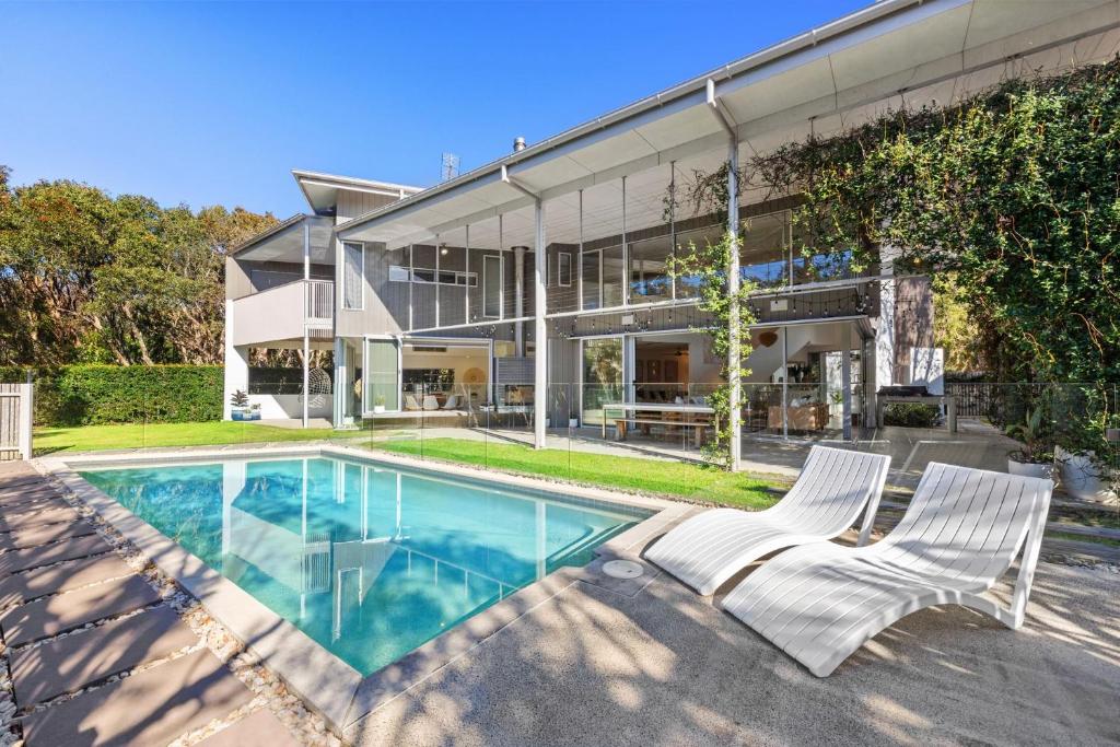 a house with a swimming pool and two white chairs at 25 Whitehaven Parade in Yaroomba