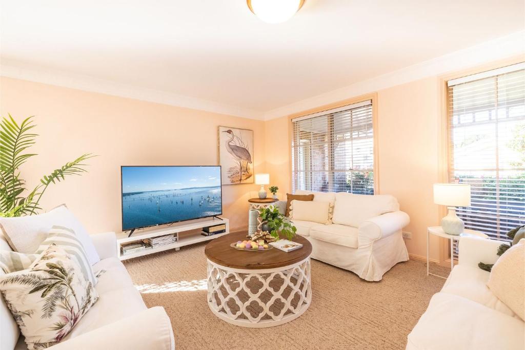 a living room with white furniture and a flat screen tv at White Sands, 14 Whitesands Road - Pet Friendly & Air Con in Fingal Bay