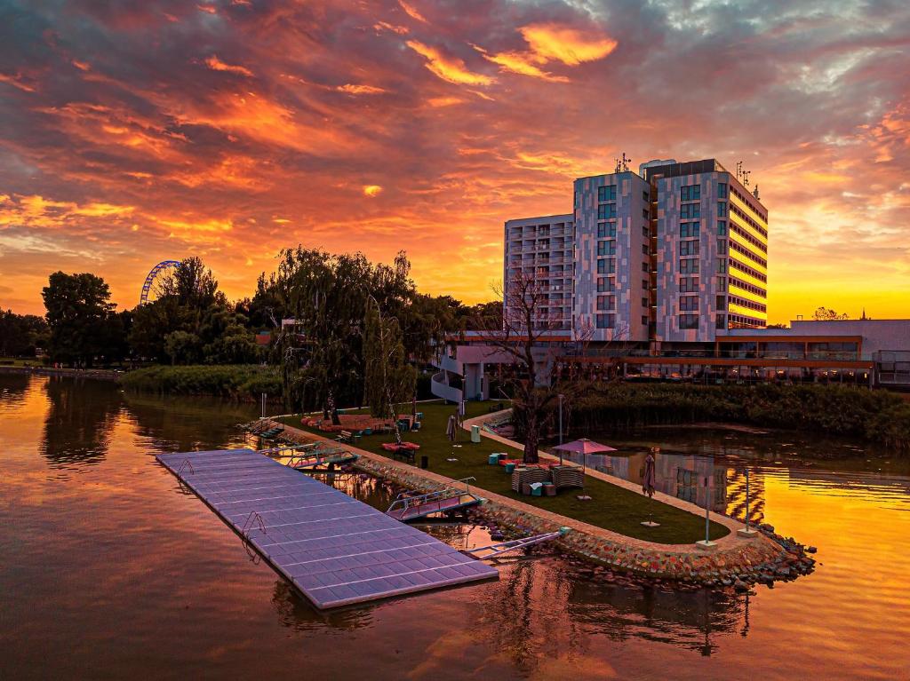 a building with solar panels in the water at sunset at Hotel Helikon, Keszthely in Keszthely