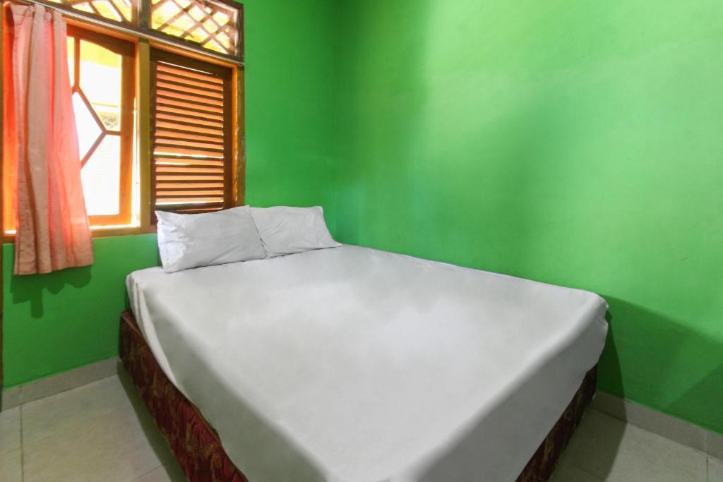 Cama blanca en una habitación verde con ventana en OYO 92908 Hotel Jayanni, en Labu Sumbawa
