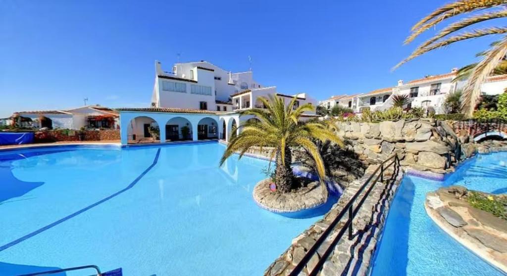 a swimming pool with a palm tree next to a building at Right by the pool area in Capistrano Village! in Nerja