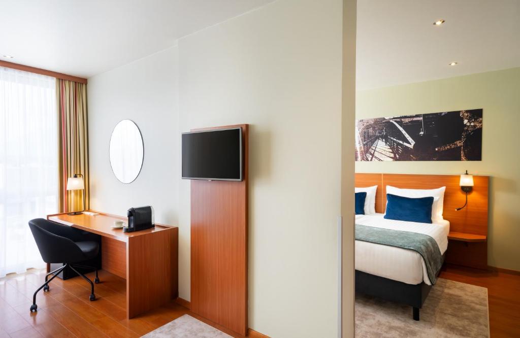 a hotel room with a bed and a desk and a tv at Leonardo Hotel Salzburg Airport in Salzburg