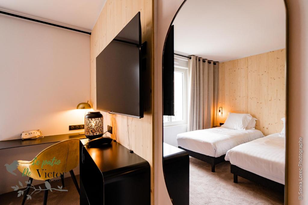 a hotel room with a bedroom with two beds and a desk at Hôtel Le Patio de Victor, Lorient in Lorient