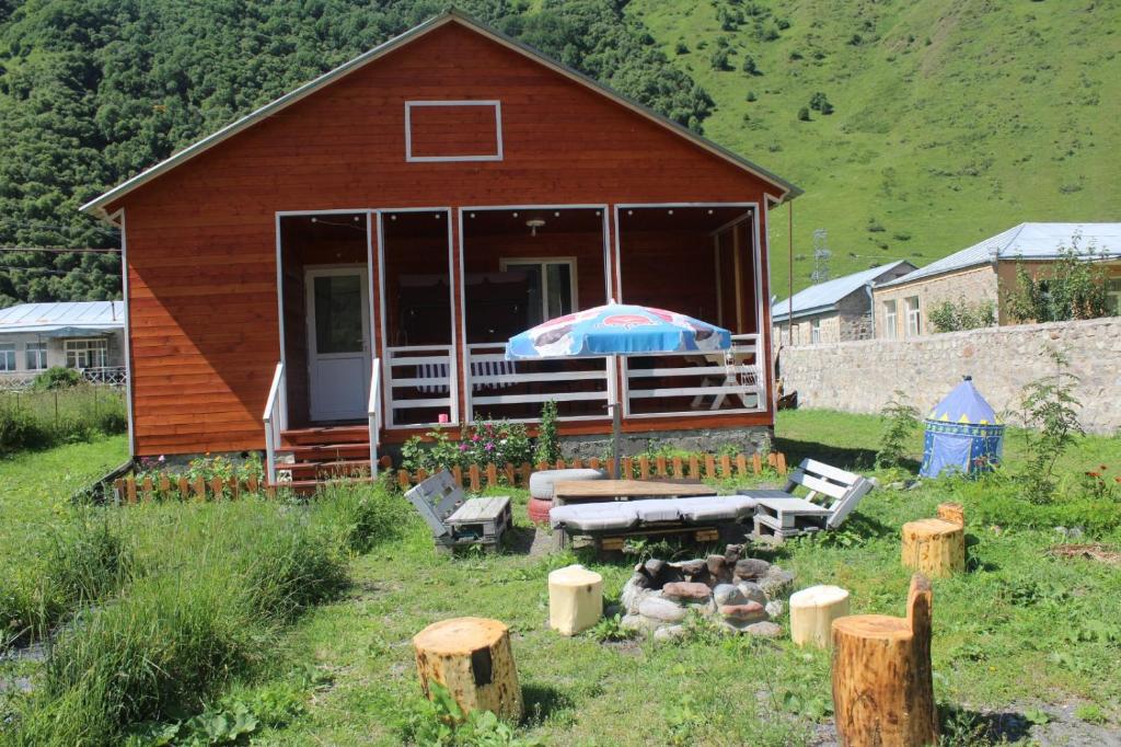 ein Haus mit einem Regenschirm und Bänken davor in der Unterkunft Warm House in Kazbegi