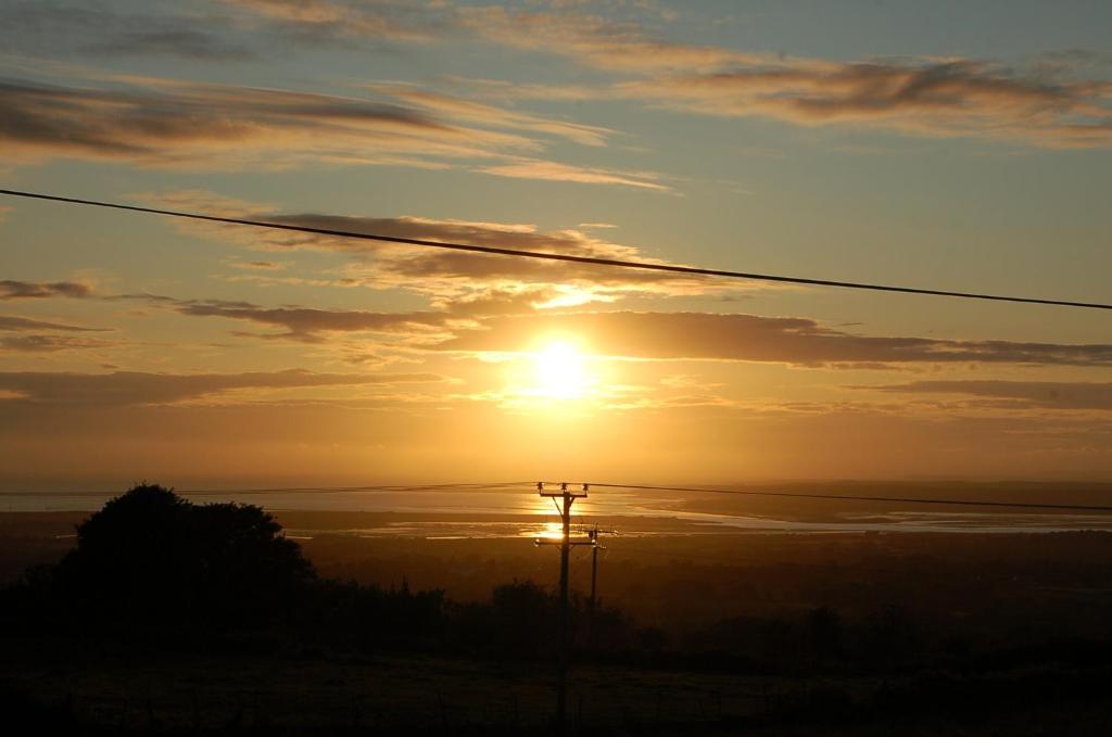 una puesta de sol sobre el océano con un poste de teléfono en Kims Retreat, en Caernarfon