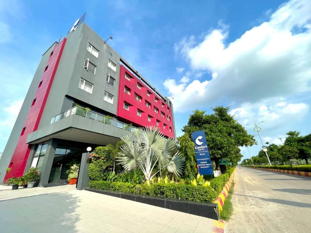 een rood en grijs gebouw met een bord ervoor bij Comfort Hotel Vista in Lucknow