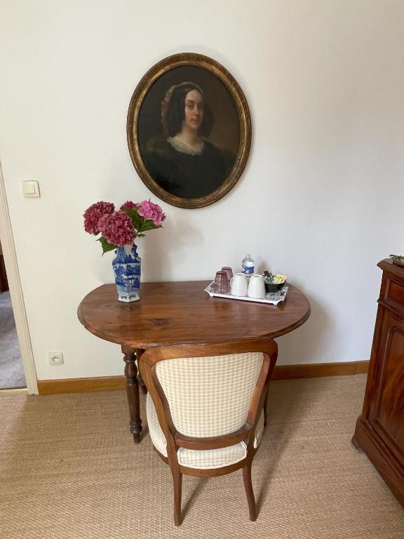 a table with a vase of flowers and a painting at Ferme de Maillezais in LʼHoumeau