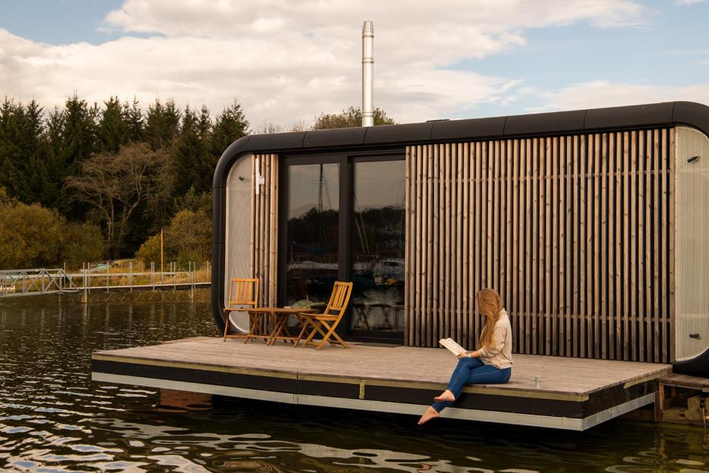 a woman sitting on a dock on a tiny house on the water at Modul Kometa in Hrdoňov