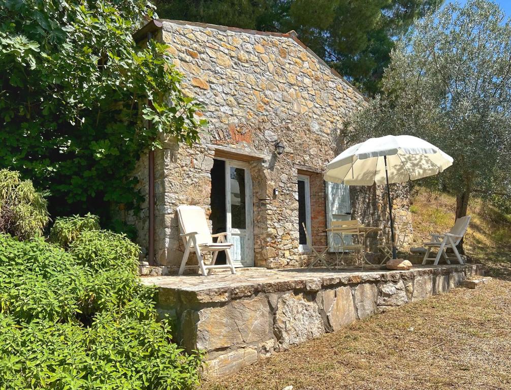 un cottage in pietra con due sedie e un ombrellone di Podere BARBI a Baschi