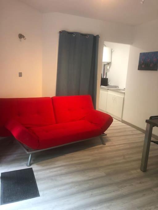 um sofá vermelho numa sala de estar com uma cozinha em Appartement en pleine forêt em Sainte-Hélène