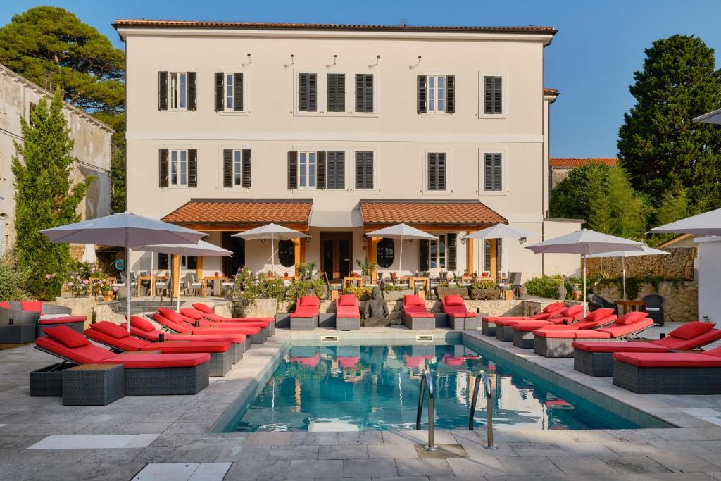 a hotel with a pool with red chairs and a building at Dolphin Suites in Veli Lošinj
