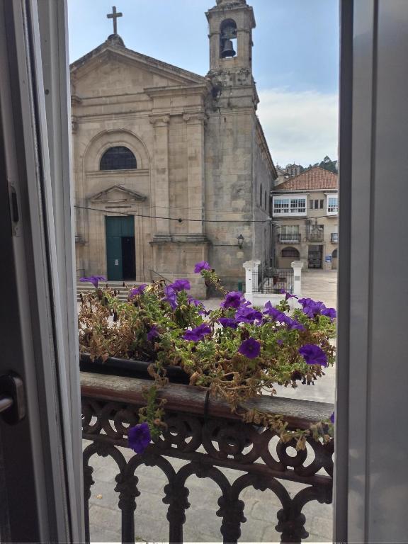 una ventana con flores púrpuras frente a una iglesia en A Parada do Camiño, en Padrón