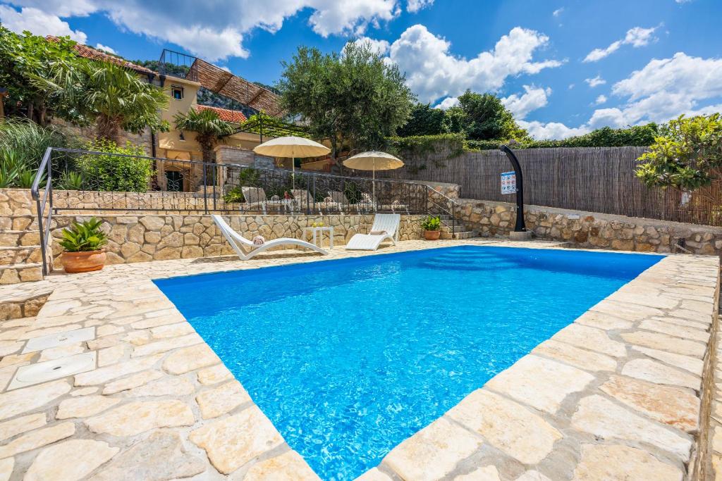 a pool with blue water in a yard with two chairs and umbrellas at Villa Cocoon - Vacation Home with Heated Pool & Garden in Bribir