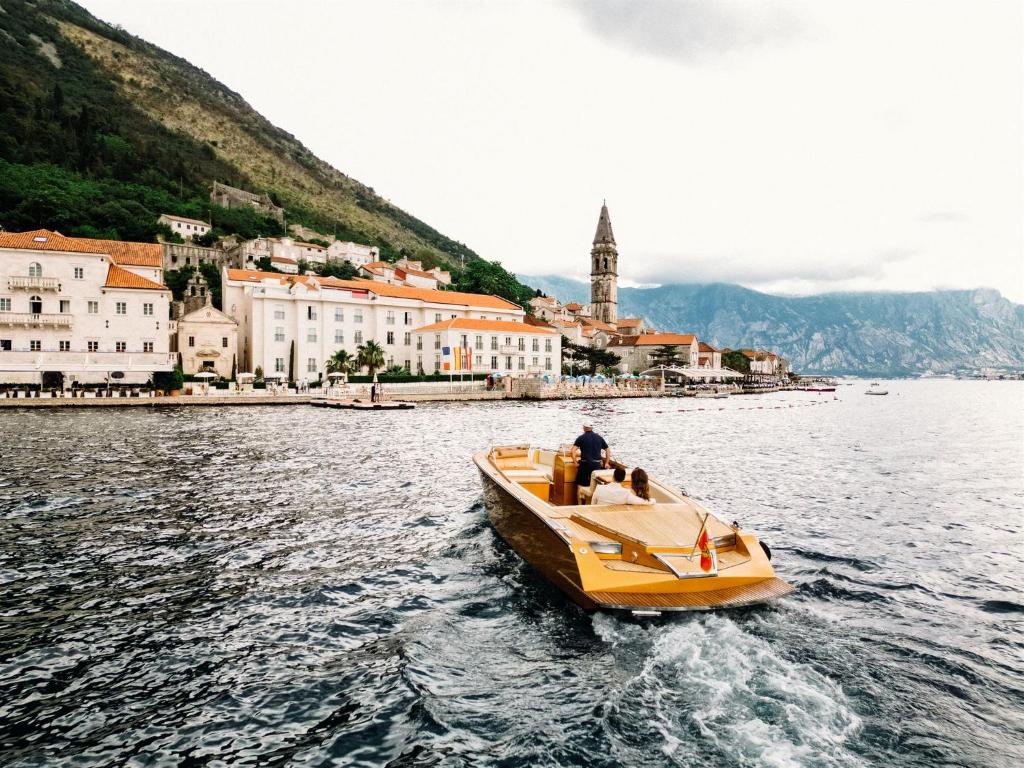 a man on a boat in the water near a city at Heritage Grand Perast By Rixos in Perast