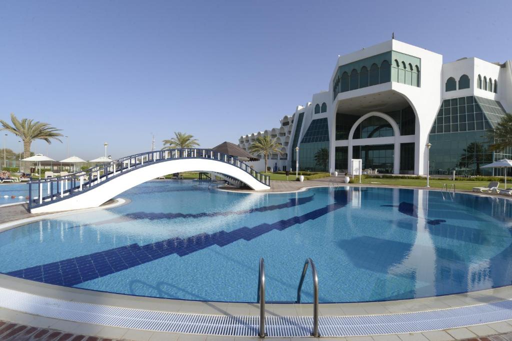 a large swimming pool with a bridge in front of a building at Mirfa Hotel in Al Mirfa