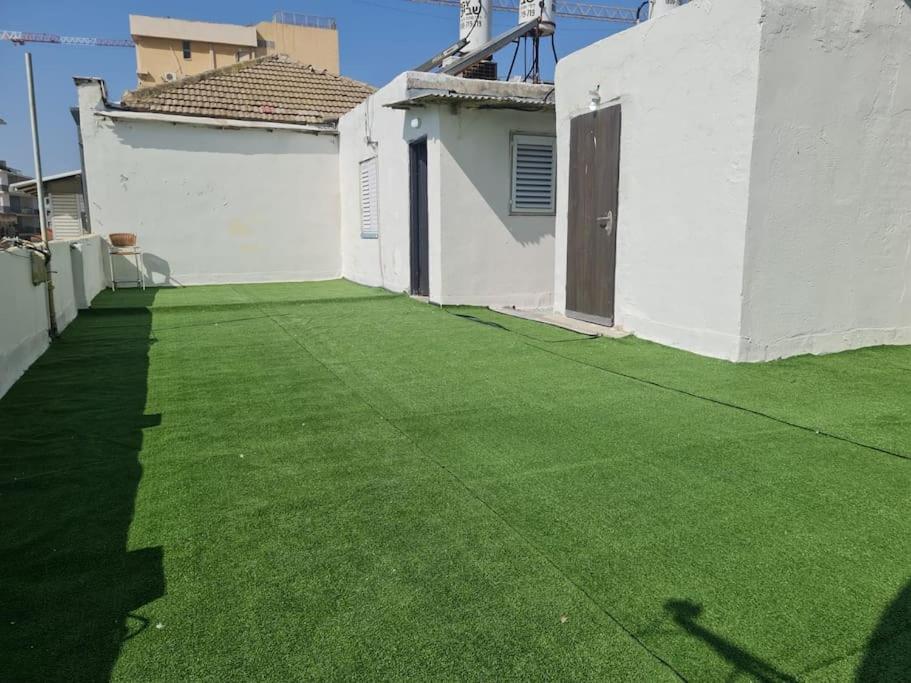 a yard with green grass next to a white building at Incredible roof in Florentin in Tel Aviv