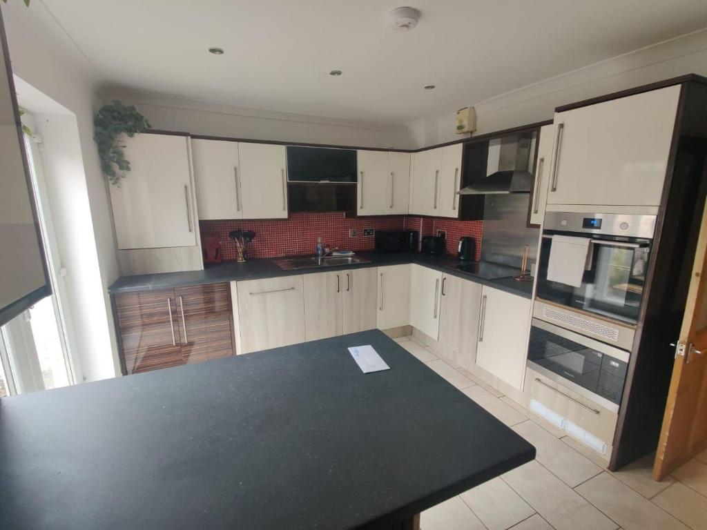 cocina con armarios blancos y encimera negra en Cosy 3-Bed house in Clydach - TV in every bedroom!, en Clydach