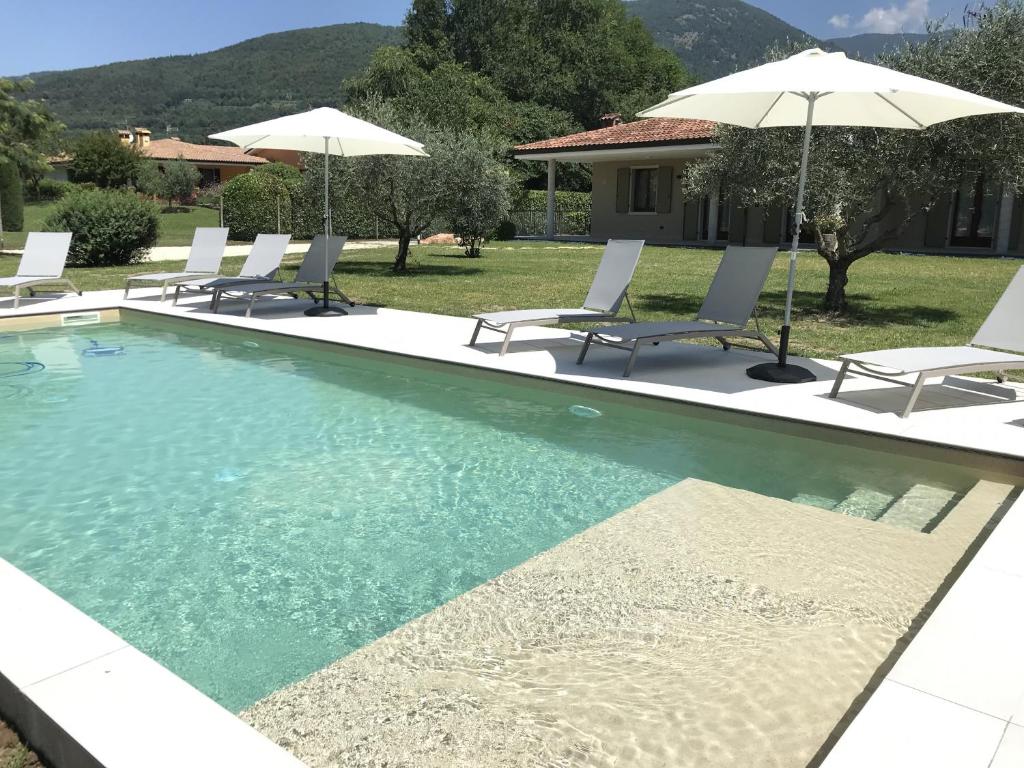 - une piscine avec des chaises longues et des parasols dans l'établissement VILLA IDA - Regarda Travel, à Costermano