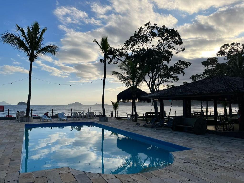 a swimming pool next to the ocean with palm trees at Summit Beach Hotel Boiçucanga in Boicucanga