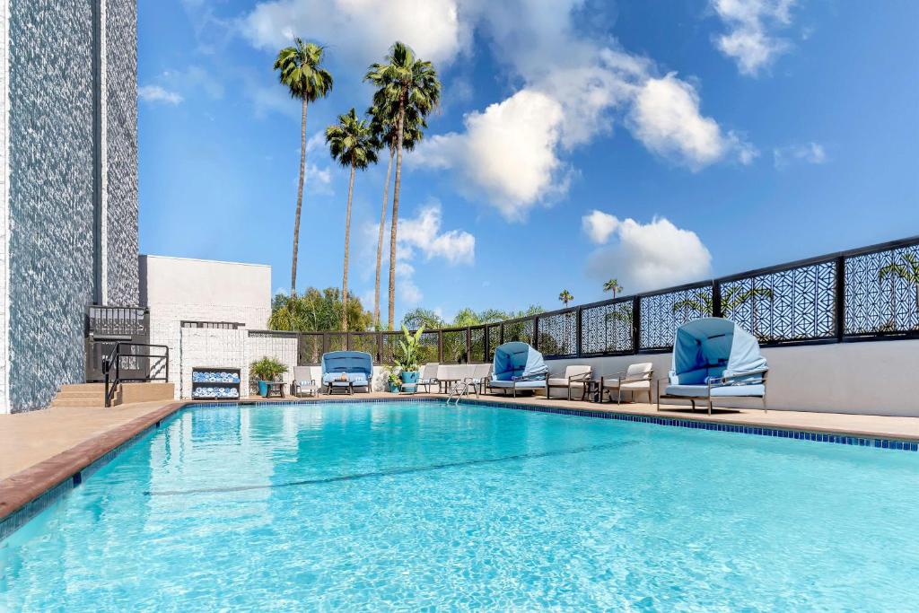uma piscina com cadeiras azuis e palmeiras em Hilton Pasadena em Pasadena