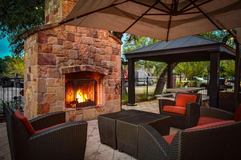 Un patio al aire libre con una chimenea de piedra con sillas y una sombrilla. en Hampton Inn & Suites Boerne, en Boerne