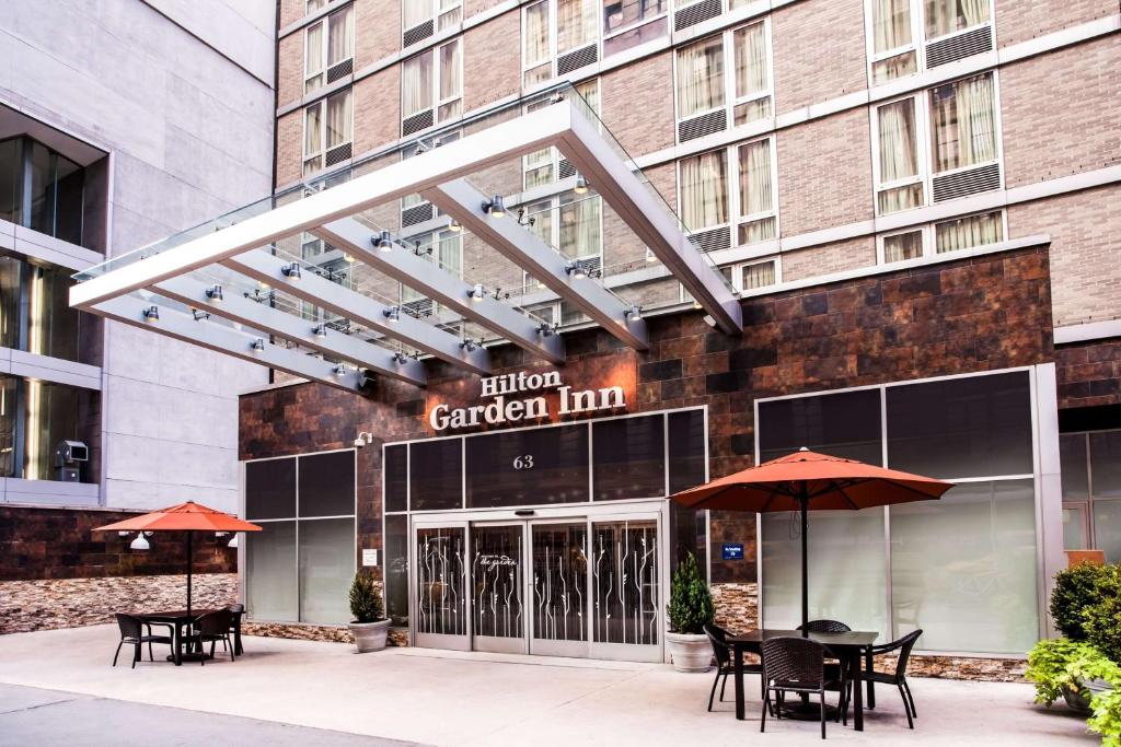 a hotel garden inn with tables and umbrellas in front of it at Hilton Garden Inn West 35th Street in New York