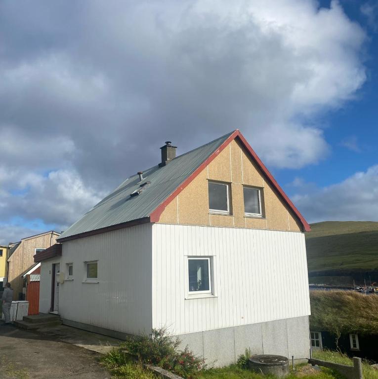 a white building with a gray roof and a house at Cosy house in the old village in Miðvágur
