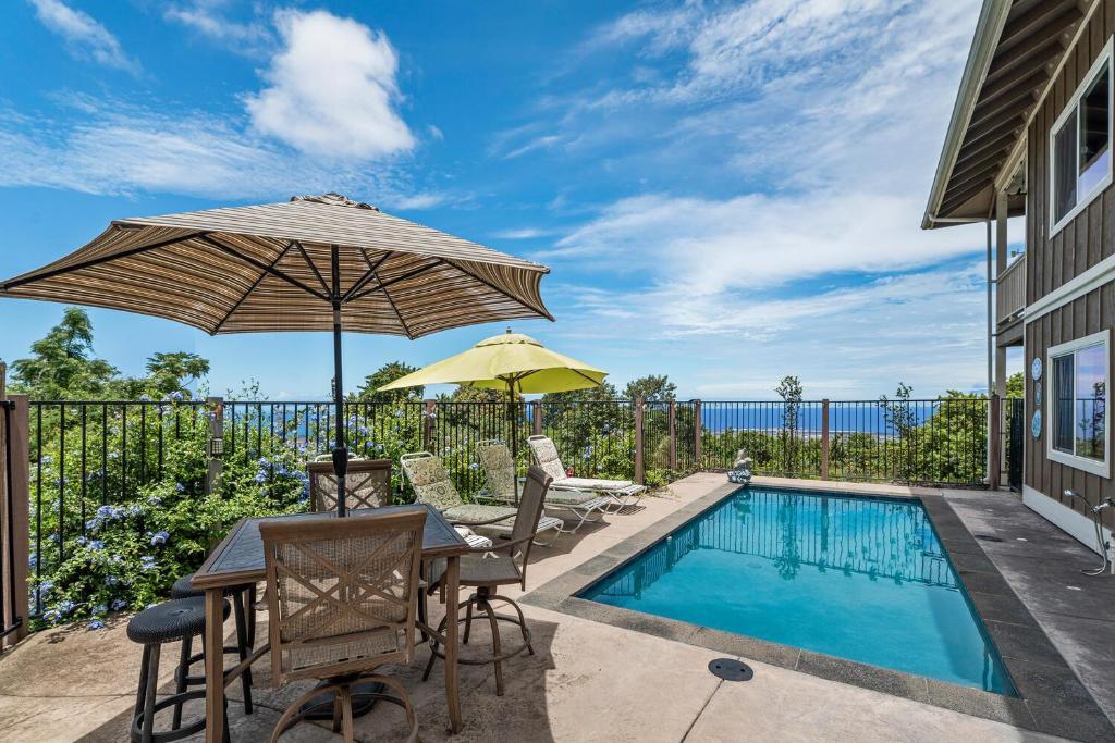 a patio with a table and umbrella and a swimming pool at Hale Lio Kai in Kailua-Kona