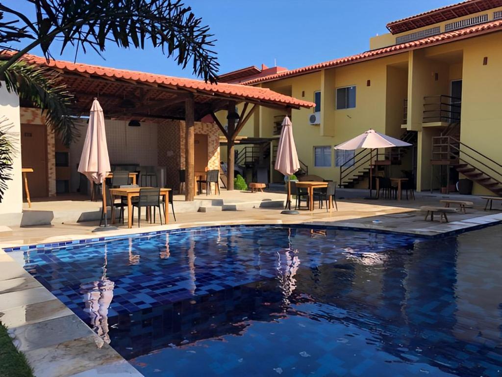 a pool in front of a house with tables and umbrellas at Apartamento Paz e Traquilidade na praia in Luis Correia