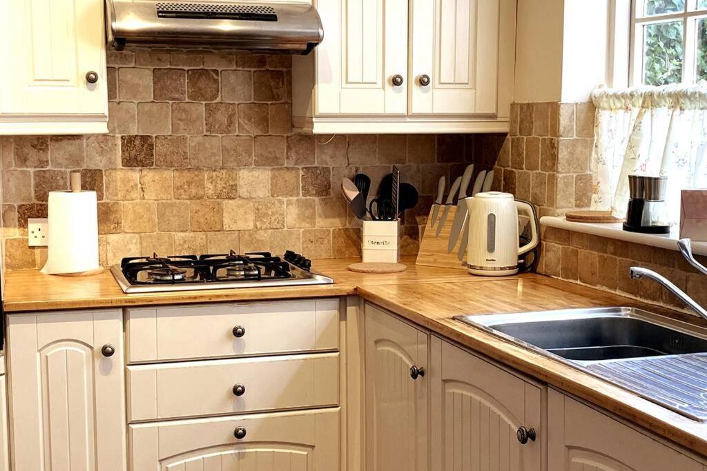 a kitchen with white cabinets and a stove and a sink at Quirky City-Centre Cottage in Exeter