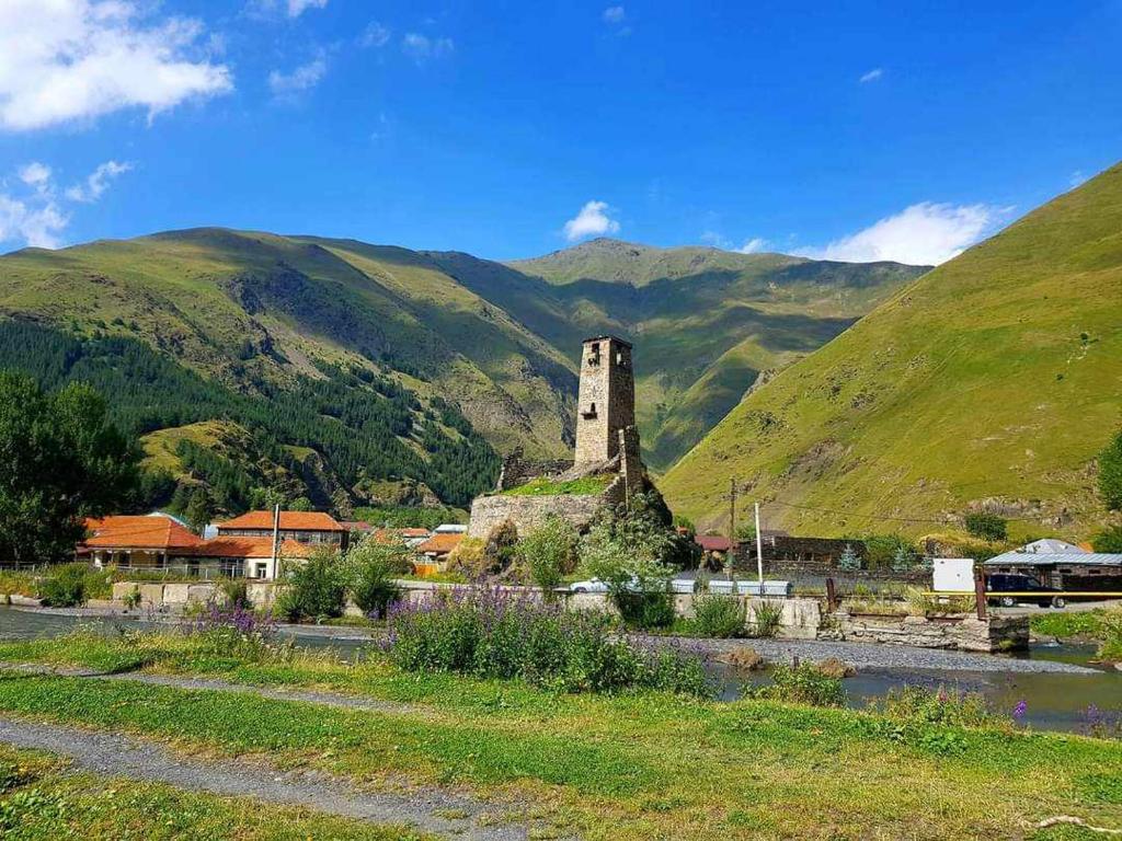 a building in the middle of a field with mountains at COZY house მყუდრო სახლი in Stepantsminda