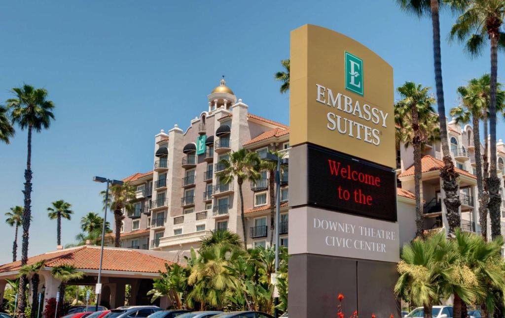 a sign in front of a hotel with palm trees at Embassy Suites by Hilton Los Angeles Downey in Downey