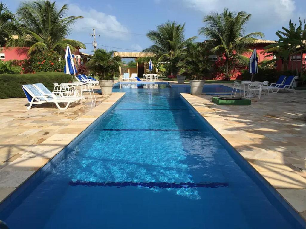 a pool with blue water and chairs and palm trees at Sonia Flats Arituba Tropical - Flat vista mar em frente à Praia de Camurupim in Nísia Floresta