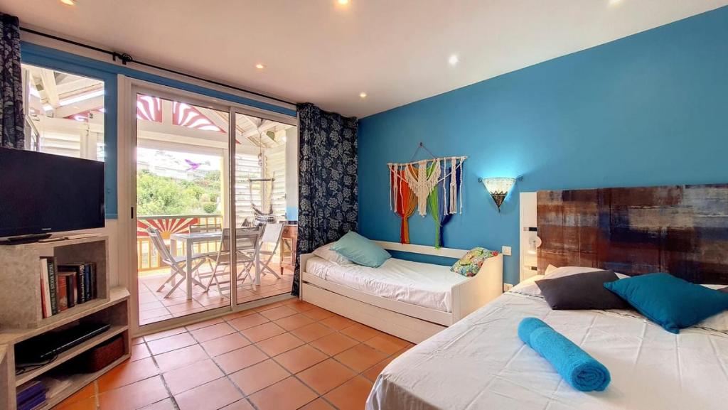 a bedroom with two beds and a television and a balcony at Appartement Varangue, Anse des rochers in Saint-François