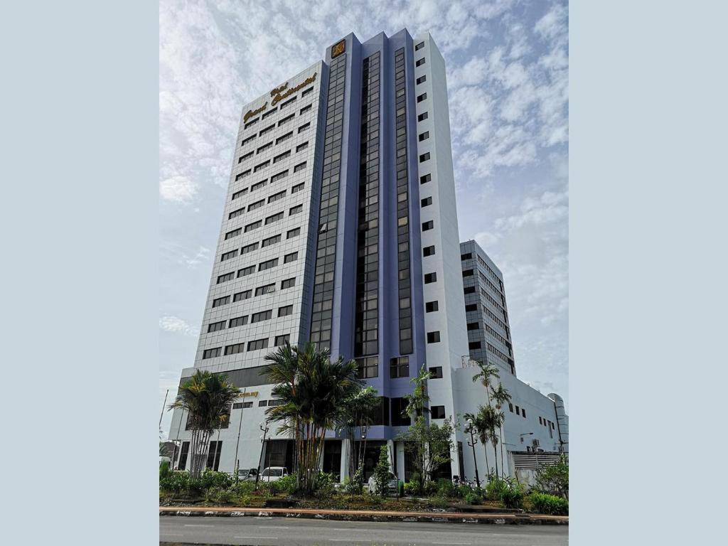 un grand bâtiment blanc avec des palmiers devant lui dans l'établissement Hotel Grand Continental Kuching, à Kuching