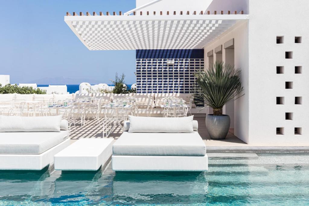 a pool with white chairs and a table and a building at Viva Nove Suites in Kamari