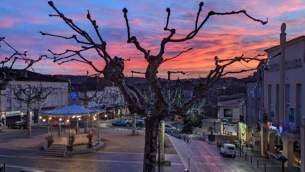 a city street with a tree with a sunset in the background at Au dessus des arcades in Vic-Fezensac