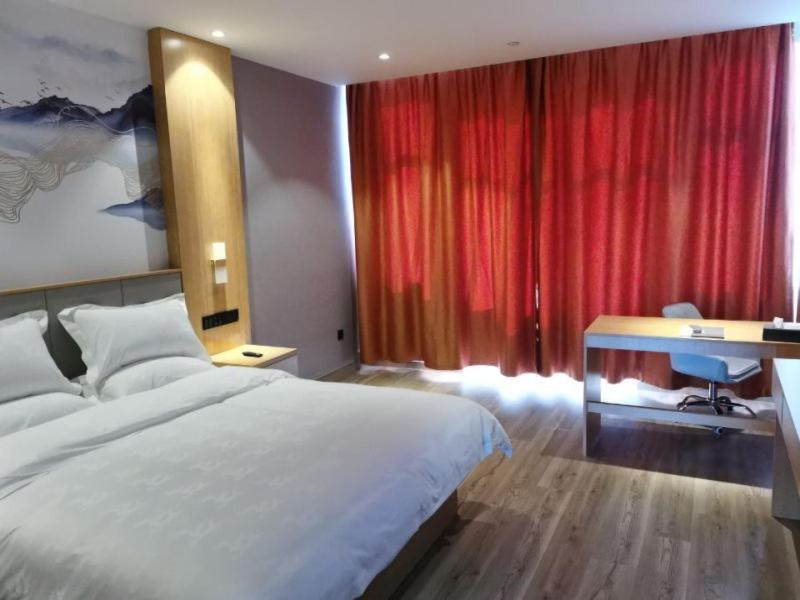 um quarto com uma cama, uma secretária e cortinas vermelhas em GreenTree Eastern Hotel Tongling Yi'an Government em Xihu
