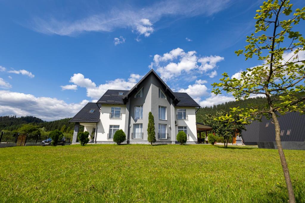une maison blanche avec un toit noir sur une cour verdoyante dans l'établissement D&D Relax SPA Bucovina, à Câmpulung Moldovenesc
