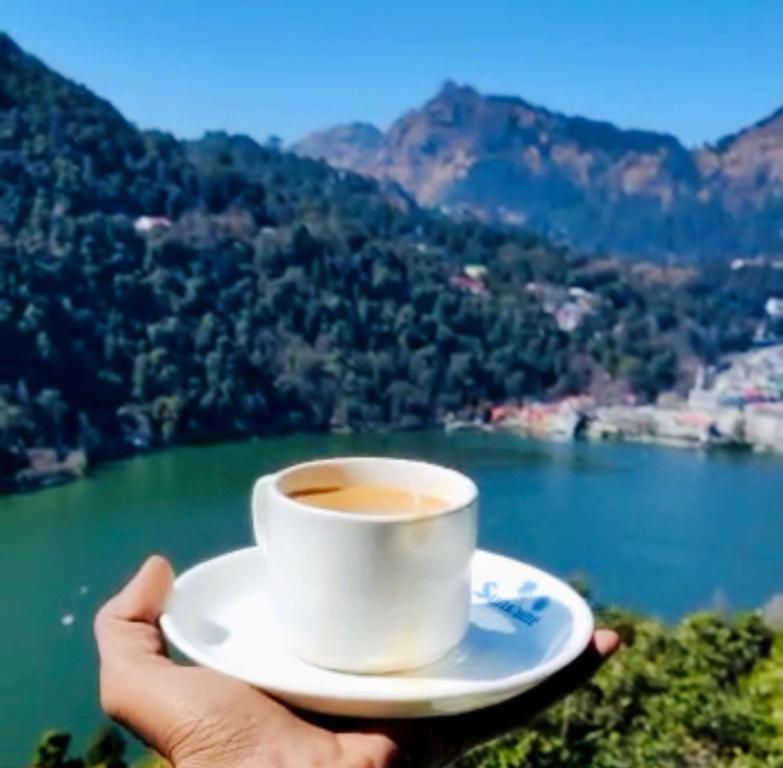 uma pessoa segurando uma xícara de café em frente a um lago em Sukoon- A Lake view BnB em Nainital
