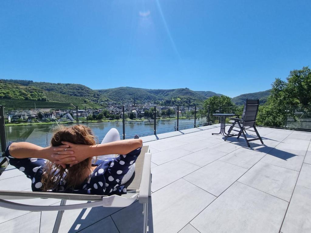 a woman sitting in a chair on a patio overlooking the water at MV Römervilla, Lofts & Penthouses mit traumhaftem Moselpanoramablick und Sauna in Treis-Karden