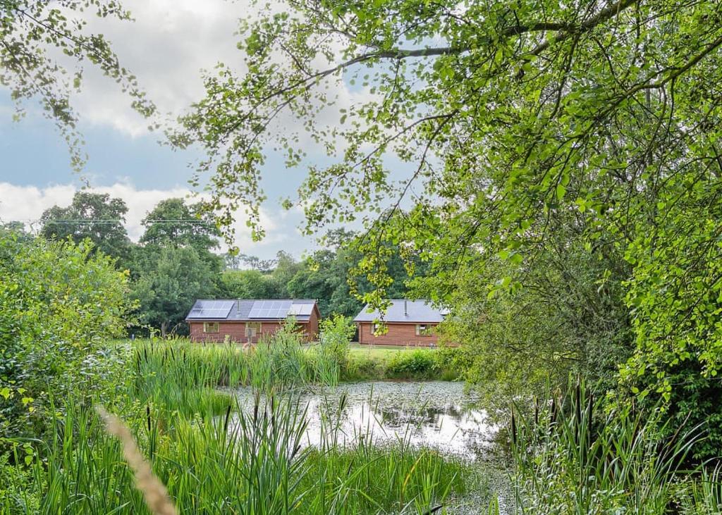 a red barn in the middle of a lake with trees at Ford Farm Lodges in Aston Ingham