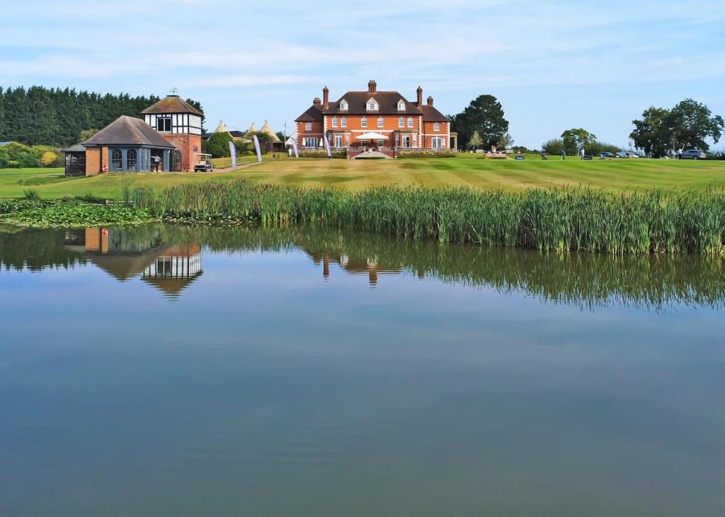 a large house on a golf course next to a lake at The Astbury Golf And Lodge Resort in Bridgnorth