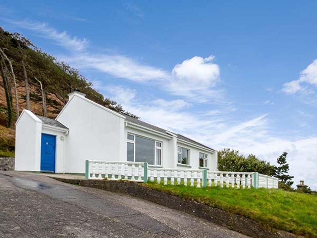 a white house with a fence next to a road at Rossbeigh Beach Cottage No 4 in Glenbeigh